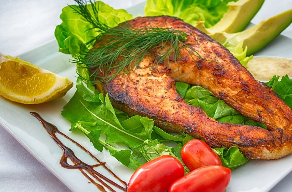 Delicious grilled salmon served with fresh vegetables and herbs on a white plate.