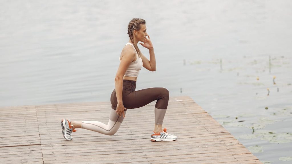 A woman performs lunges on a lakeside wooden deck, showcasing a fit lifestyle outdoors.