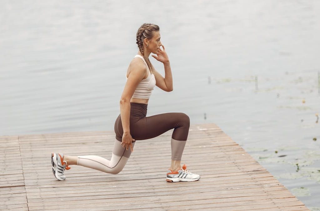 A woman performs lunges on a lakeside wooden deck, showcasing a fit lifestyle outdoors.